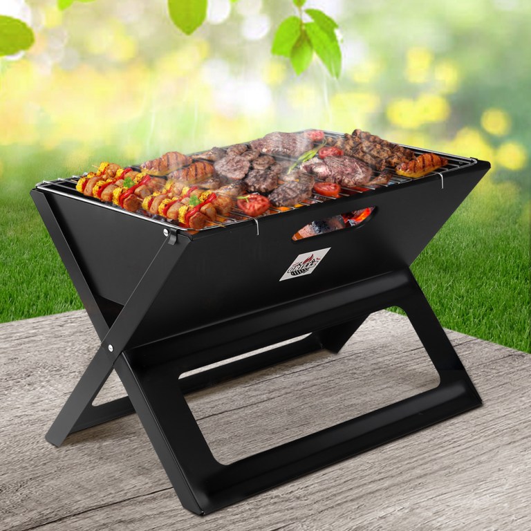 Portable BBQ with grilled meat and veggies outdoors.