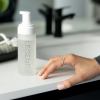 cleansing mousse | makeup removal | deep cleansing | nourishing Hand near skincare bottle on bathroom sink.