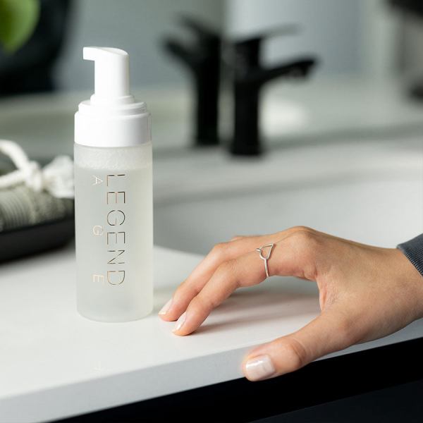 cleansing mousse | makeup removal | deep cleansing | nourishing Hand near skincare bottle on bathroom sink.