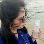 Woman holding skincare bottle on the beach.