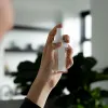 emulsion spray | triple action | super moisturizing | acne & spot removal Hand holding a clear spray bottle indoors.