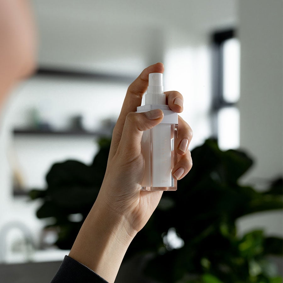 Hand holding a clear spray bottle indoors.