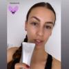 Person holding skincare product tube, smiling selfie