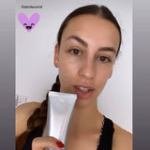Person holding skincare product tube, smiling selfie