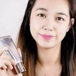Woman holding skincare product tube smiling.