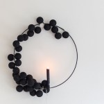 Black wreath with spheres and candle on wall.