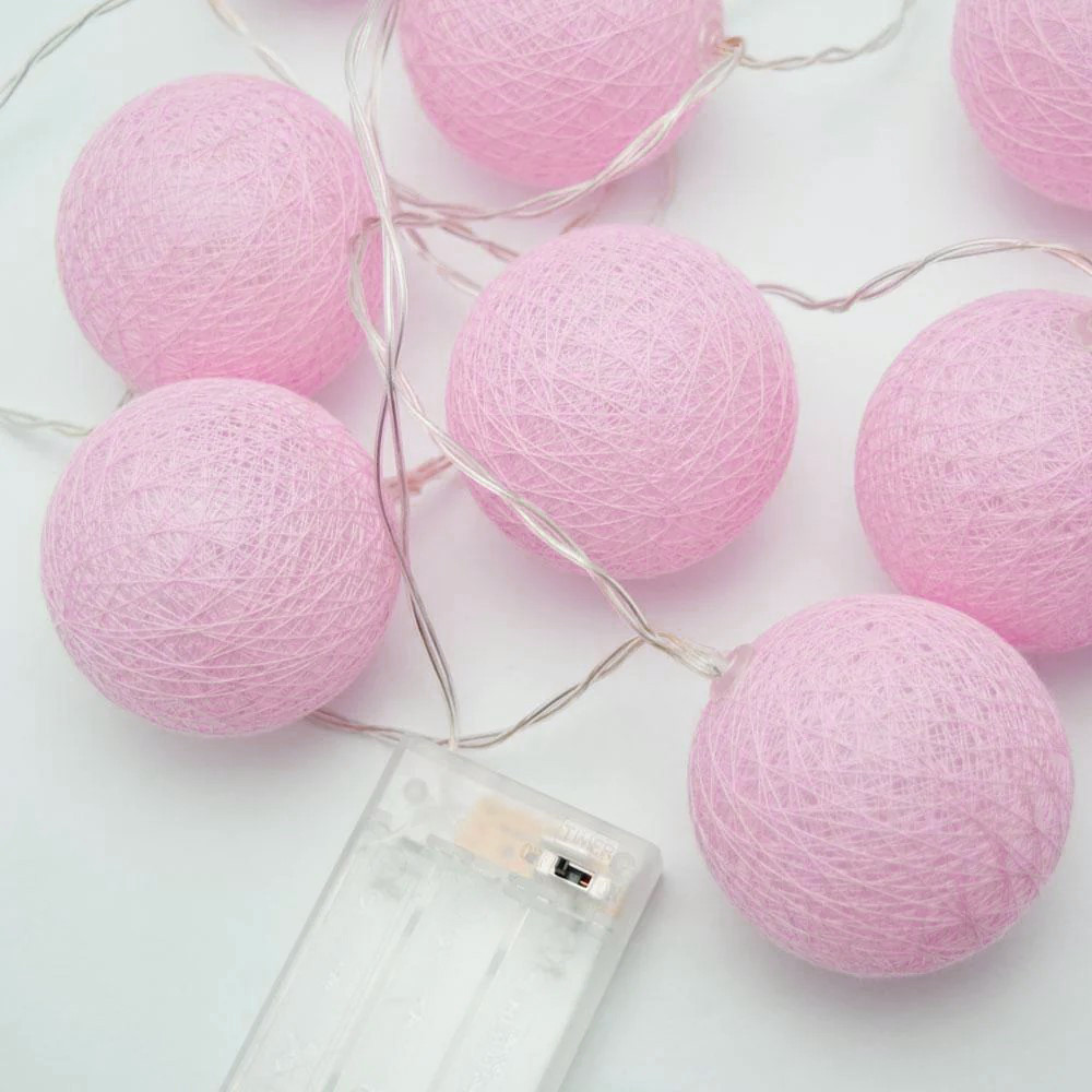 Pink cotton ball string lights on white background.
