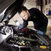Mechanic inspecting car engine with flashlight.