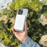 laser 5000mah magnetic wireless power bank white Hand holding smartphone with charger in garden backdrop.