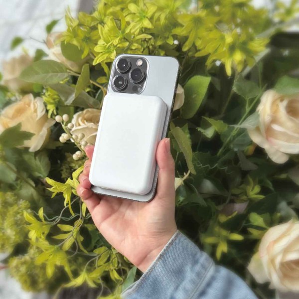 laser 5000mah magnetic wireless power bank white Hand holding smartphone with charger in garden backdrop.