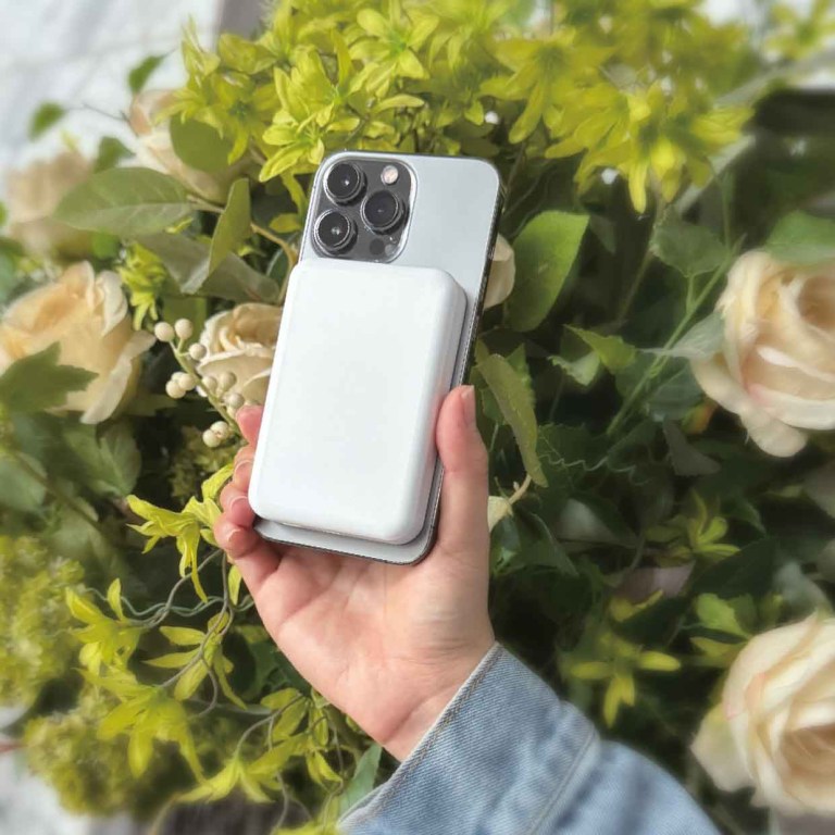 laser 5000mah magnetic wireless power bank white Hand holding smartphone with charger in garden backdrop.