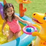 Child playing in inflatable pool with dinosaur toy.