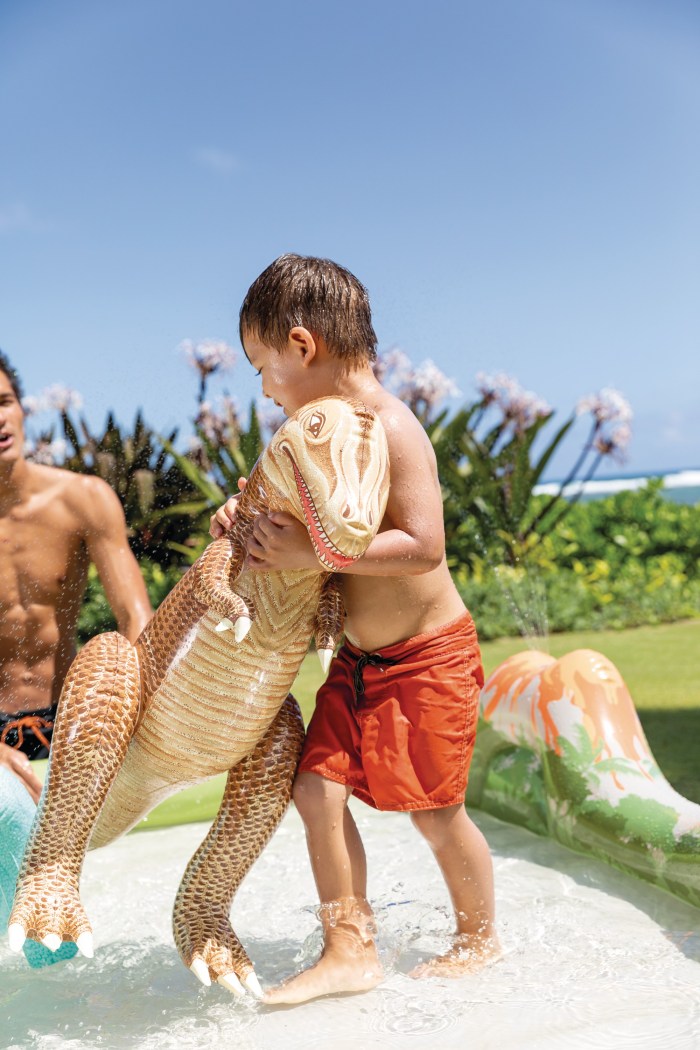 Child in pool with inflatable dinosaur toy.