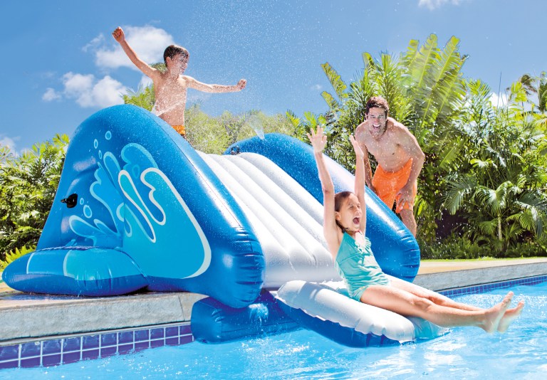 Kids playing on inflatable water slide at pool.