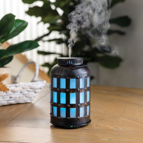 Blue illuminated diffuser releasing mist on table.