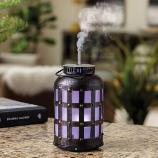 Decorative metal lantern diffuser emitting steam on table.
