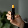 Person holding orange lipstick with patterned case.