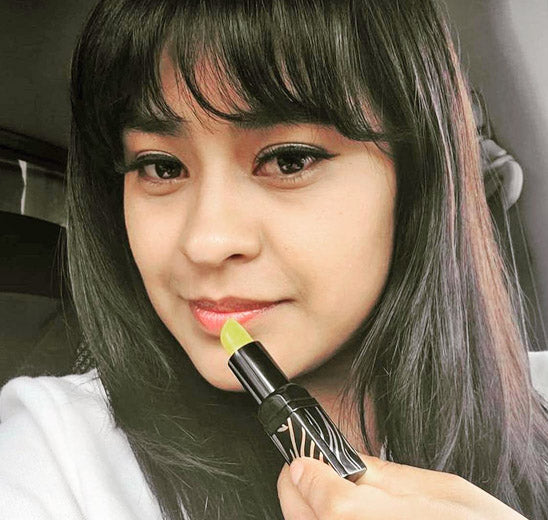 Woman applying green lipstick, close-up view.