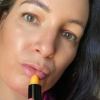Woman applying orange lipstick, close-up face view.