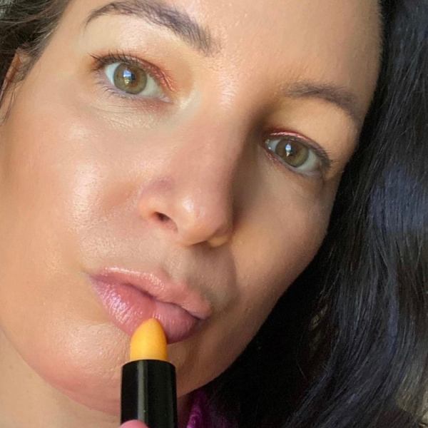 Woman applying orange lipstick, close-up face view.