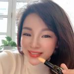 Person holding a lipstick, smiling indoors.