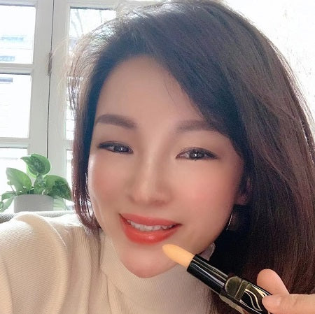 Person holding a lipstick, smiling indoors.