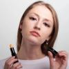 Woman holding yellow lip balm, demonstrating application.