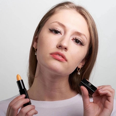 Woman holding yellow lip balm, demonstrating application.