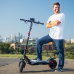 Smiling man posing with electric scooter outdoors.