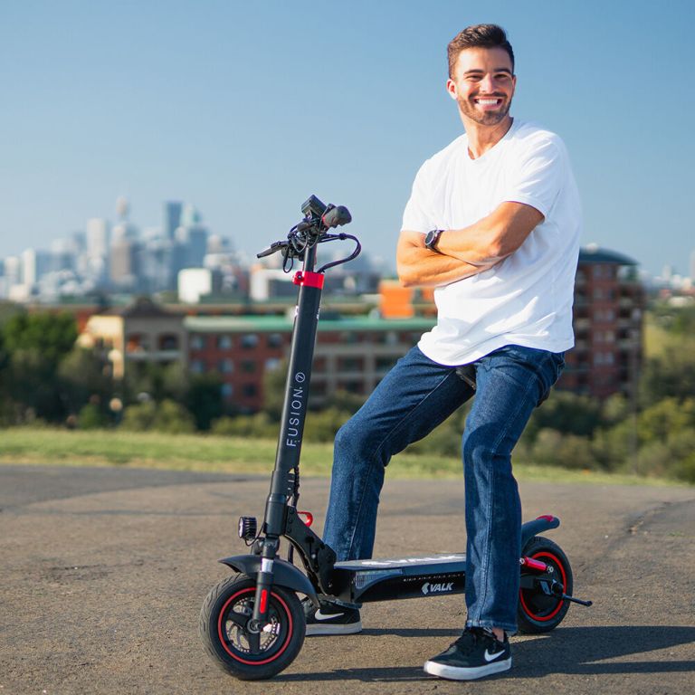 Smiling man on electric scooter with city skyline.
