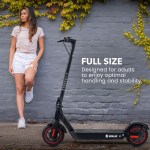 Woman standing by electric scooter with leafy wall.
