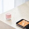 Pink speaker beside smartphone with playlist screen.