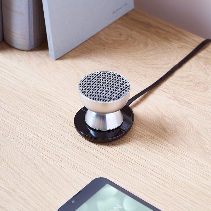 lexon tamo infinitely pairable bluetooth speaker alu polish Compact silver speaker charging on wooden desk.