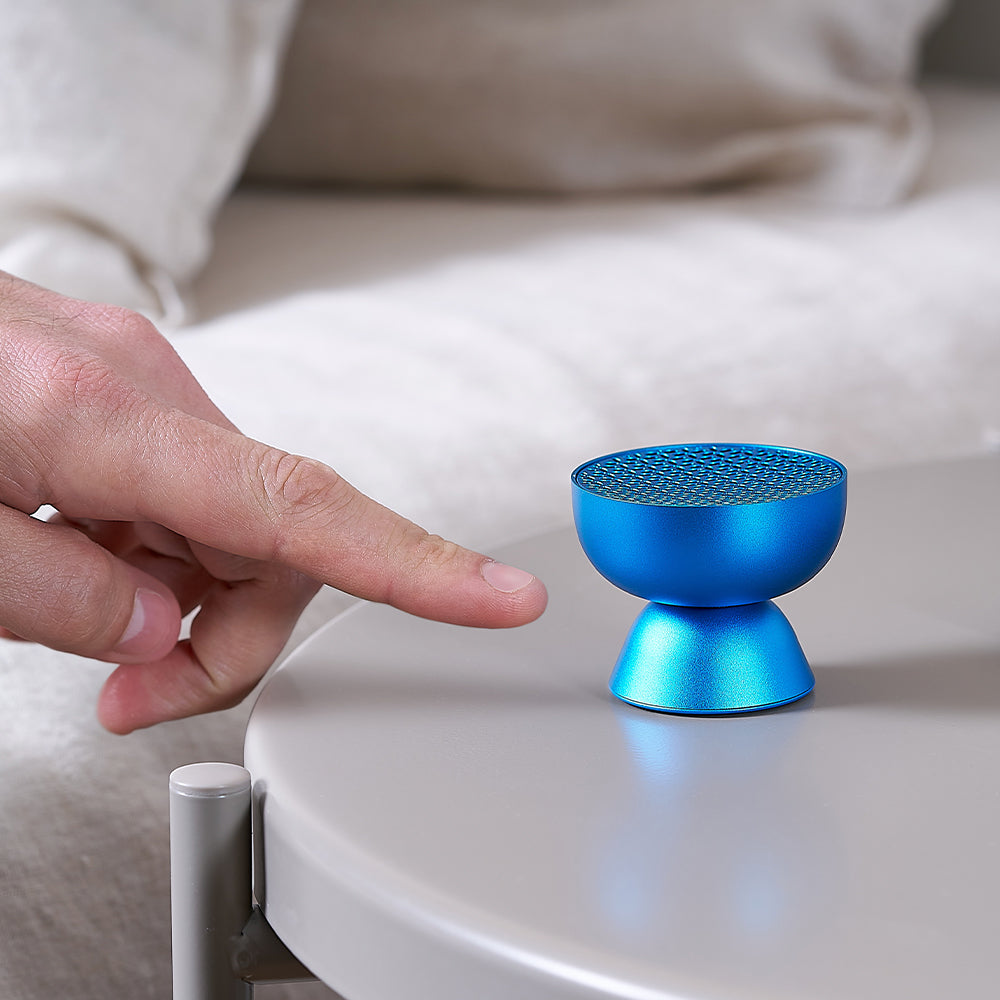 Blue mini speaker on table near a hand.