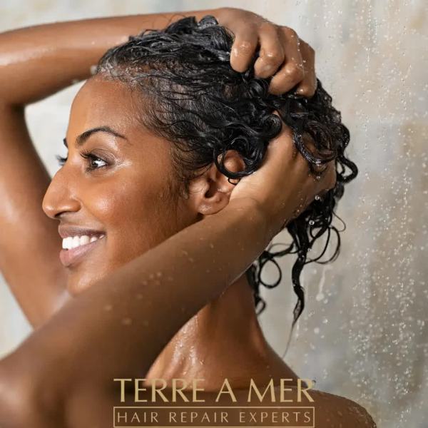 Woman washing hair under shower, smiling.