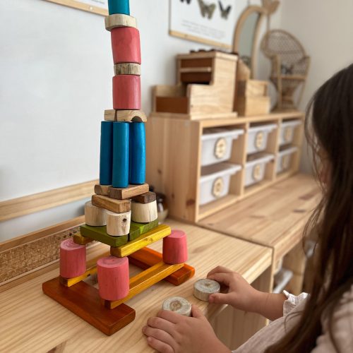 Child building colourful wooden block tower.