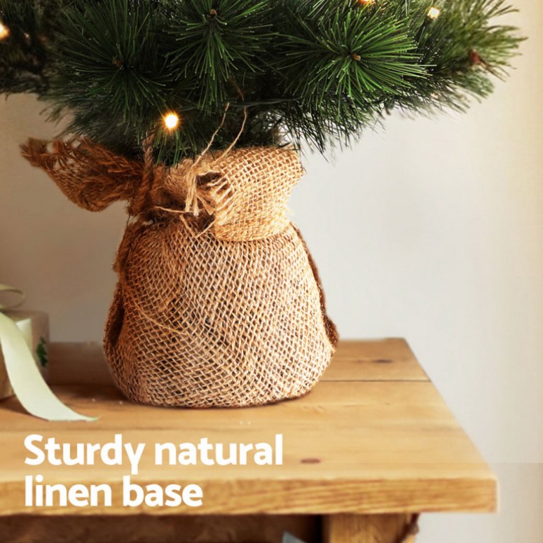 jingle jollys christmas tree 60cm mini tabletop 8 light modes timer xmas tree Christmas tree with linen wrapped base on table.