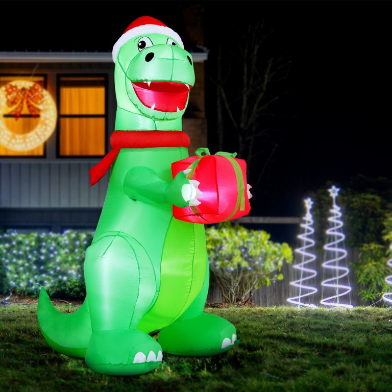 Inflatable Christmas dinosaur with gift in festive lights.