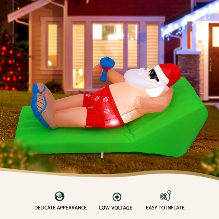 Inflatable Santa lounging on green chair in yard.