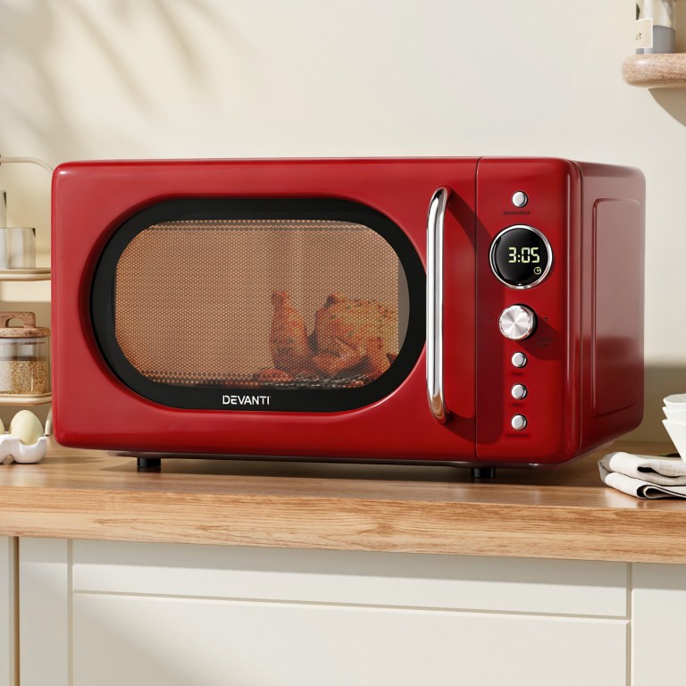 Red microwave with chicken inside on kitchen bench.