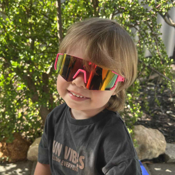 Child smiling with colourful sunglasses outdoors.