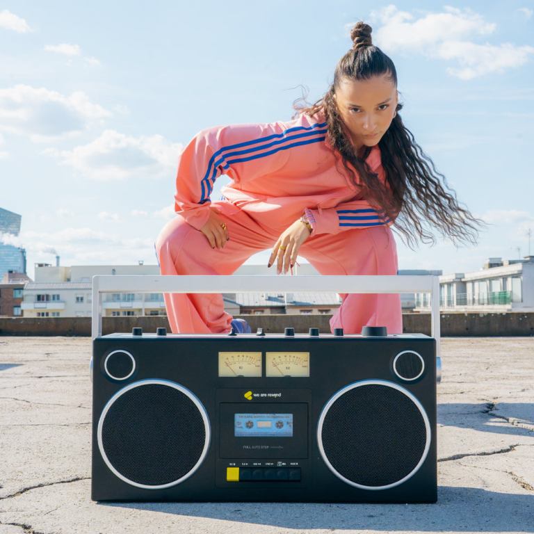 Woman in pink tracksuit with boombox outdoors.