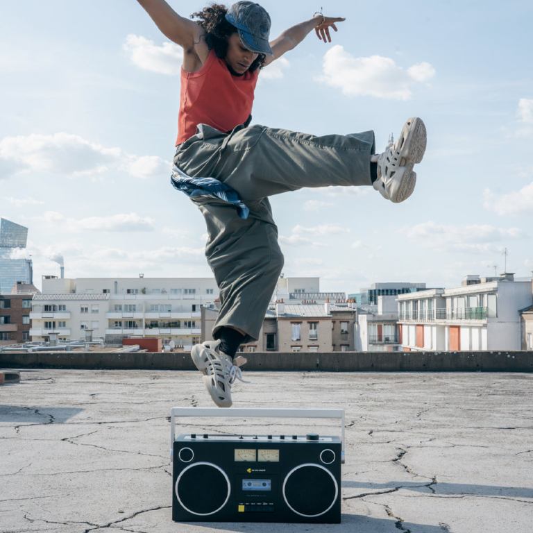 Person dances energetically on rooftop with boombox.