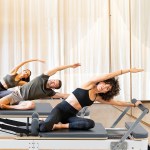 Group doing Pilates side stretches on reformers.