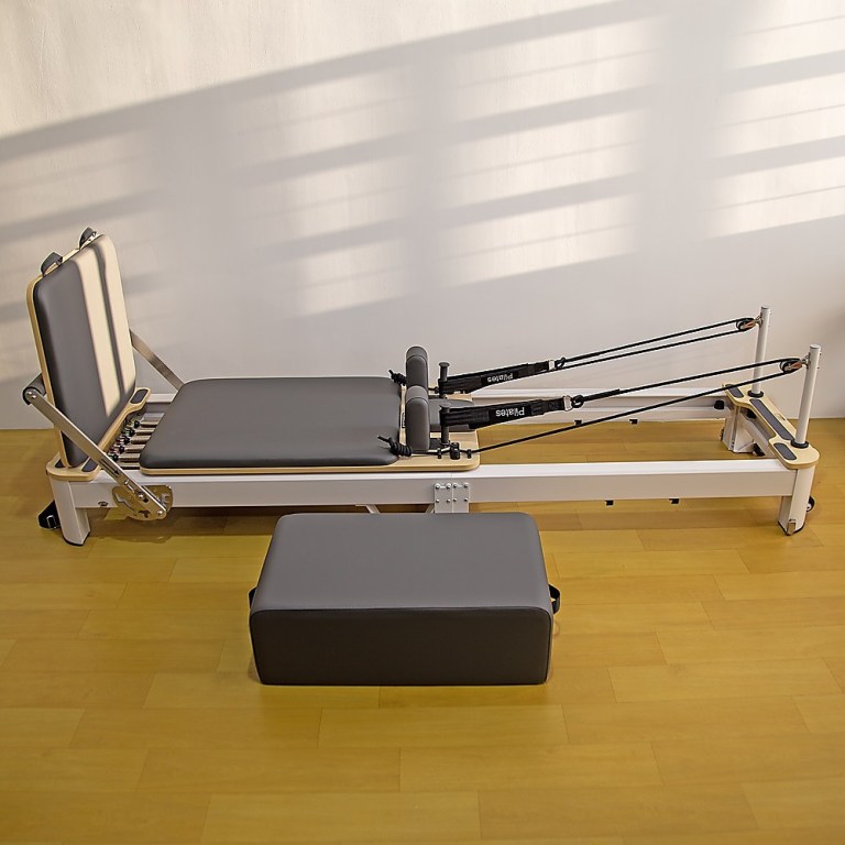 Pilates reformer machine on wooden floor.