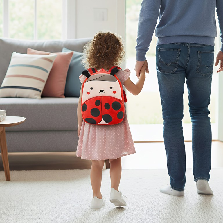 Child with ladybug backpack holding adult’s hand