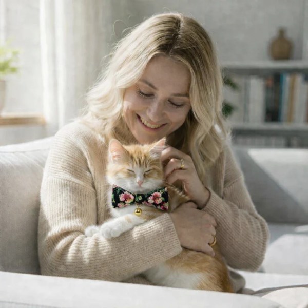 Woman cuddling ginger cat wearing floral bow tie