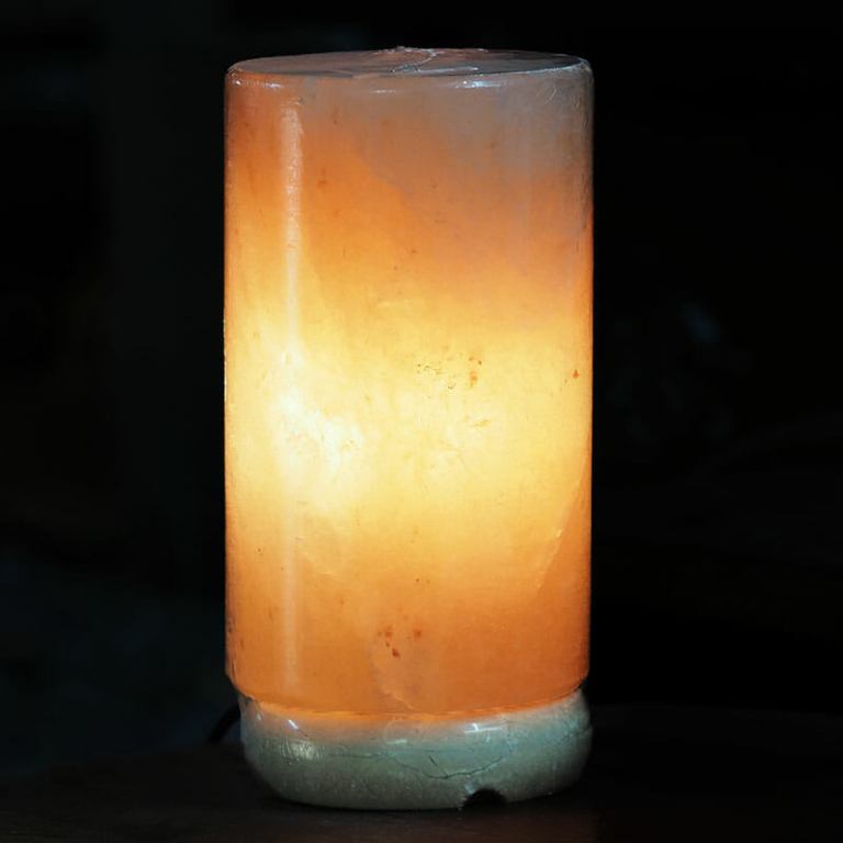 Glowing cylindrical Himalayan salt lamp on dark background
