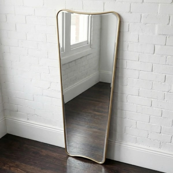 Gold-framed wavy mirror against white brick wall