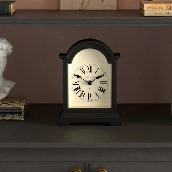 Black mantel clock with Roman numerals on shelf